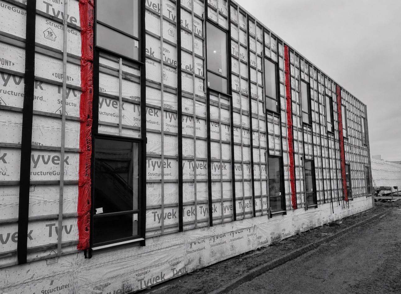 Modular facade clad in Tyvek breather membrane with window openings framed in black